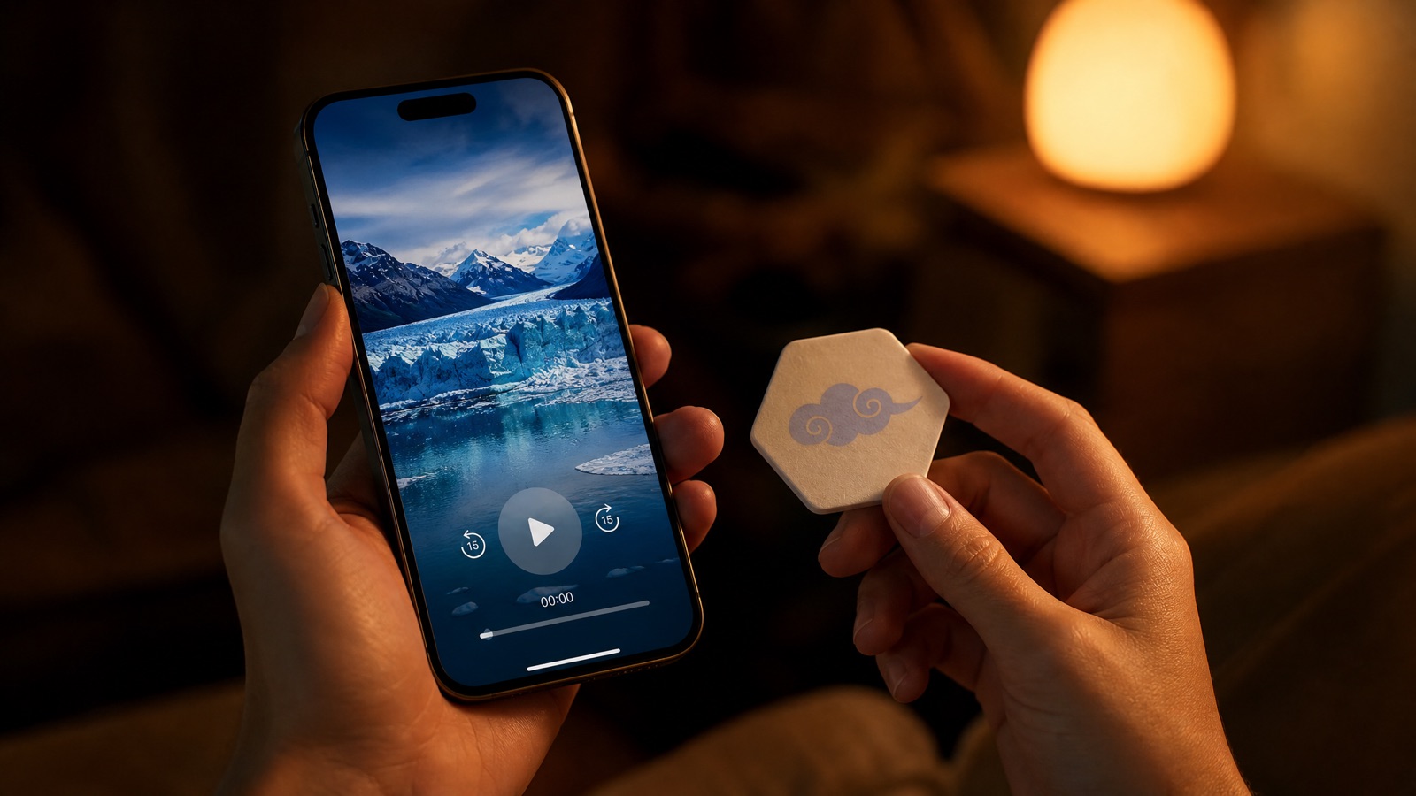 Hands holding a scent patch and a phone playing a glacier scene by warm lamplight